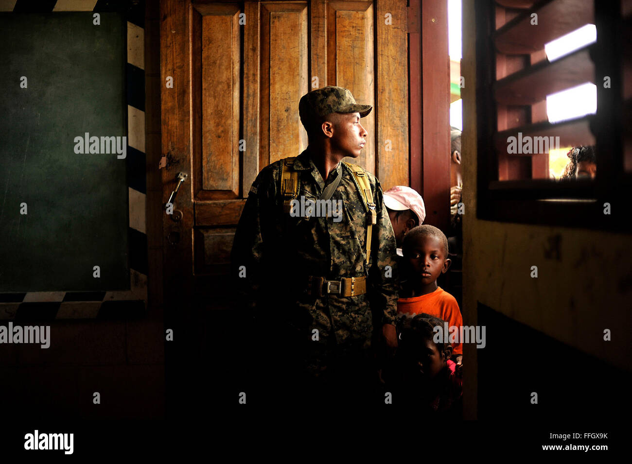 A couple of young children peek around a Honduran soldier standing guard as doctors from the Joint Task Force-Bravo Medical Element tend to patients. Stock Photo