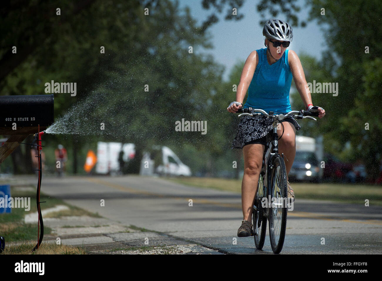 A RAGBRAI participant passes through a stream of water set out by a local resident of Lake View, Iowa. The temperatures each day rose past 100 degrees, and many of the residents set up garden hoses to cool off the passing cyclists. Stock Photo