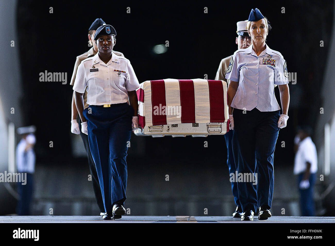U.S. Army Pfc. Shantilla Robinson, (left front) U.S. Air Force Chief Master Sgt. Laura Noel, (right front) U.S. Navy Petty Officer 3rd Class India Davis (back left) and U.S. Marine Cassie McDole (back right) escort a flag-draped transfer case from a U.S. Air Force C-17 Globemaster III during the U.S. Joint POW/MIA Accounting Command Arrival Ceremony, Nov. 30, 2012, at Joint Base Pearl Harbor-Hickam. Stock Photo