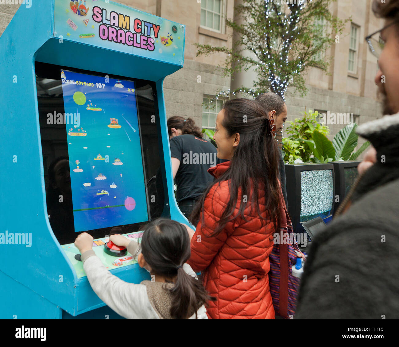 Asian mother and daughter playing Slam City Oracles video arcade game - USA Stock Photo