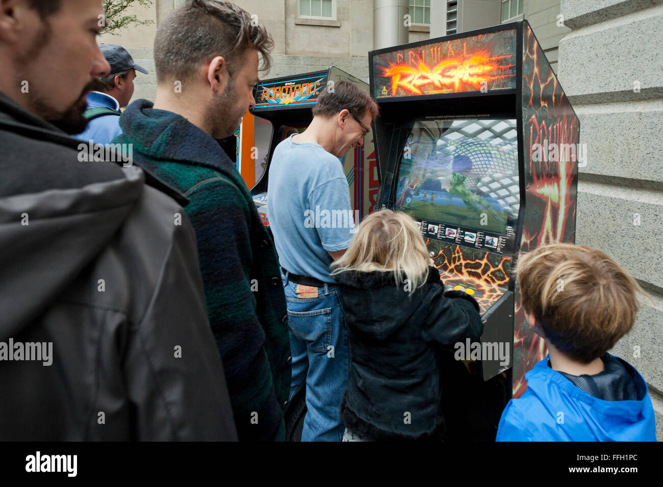 Man playing arcade video game with daughter - USA Stock Photo