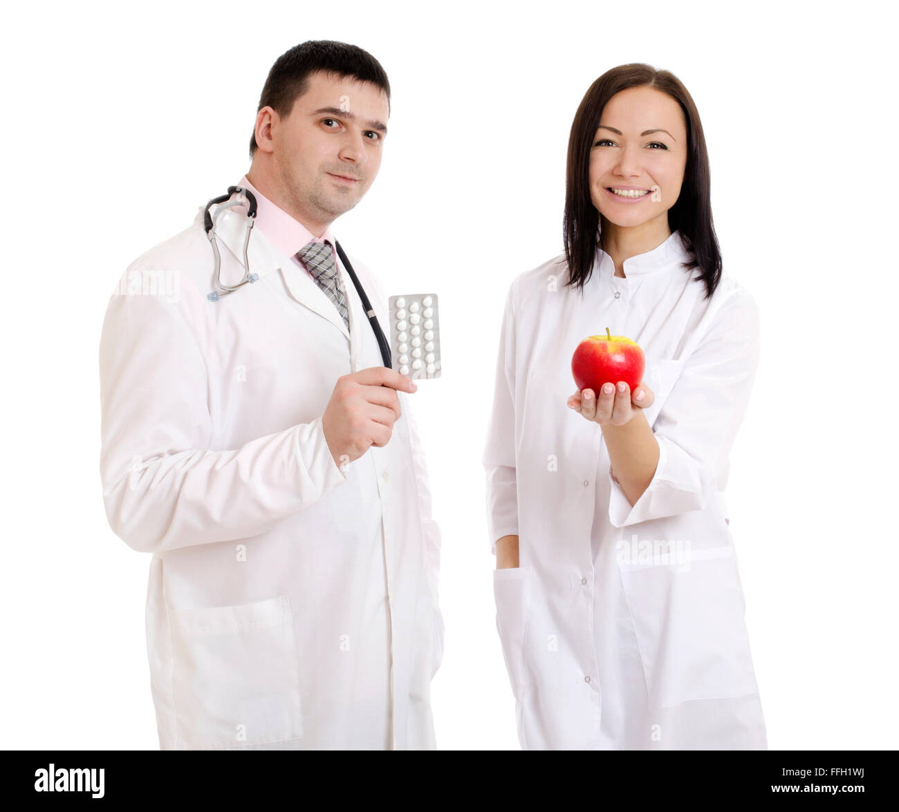 Male and female doctors holding apple and bunch of tablets isolated on white background Stock Photo