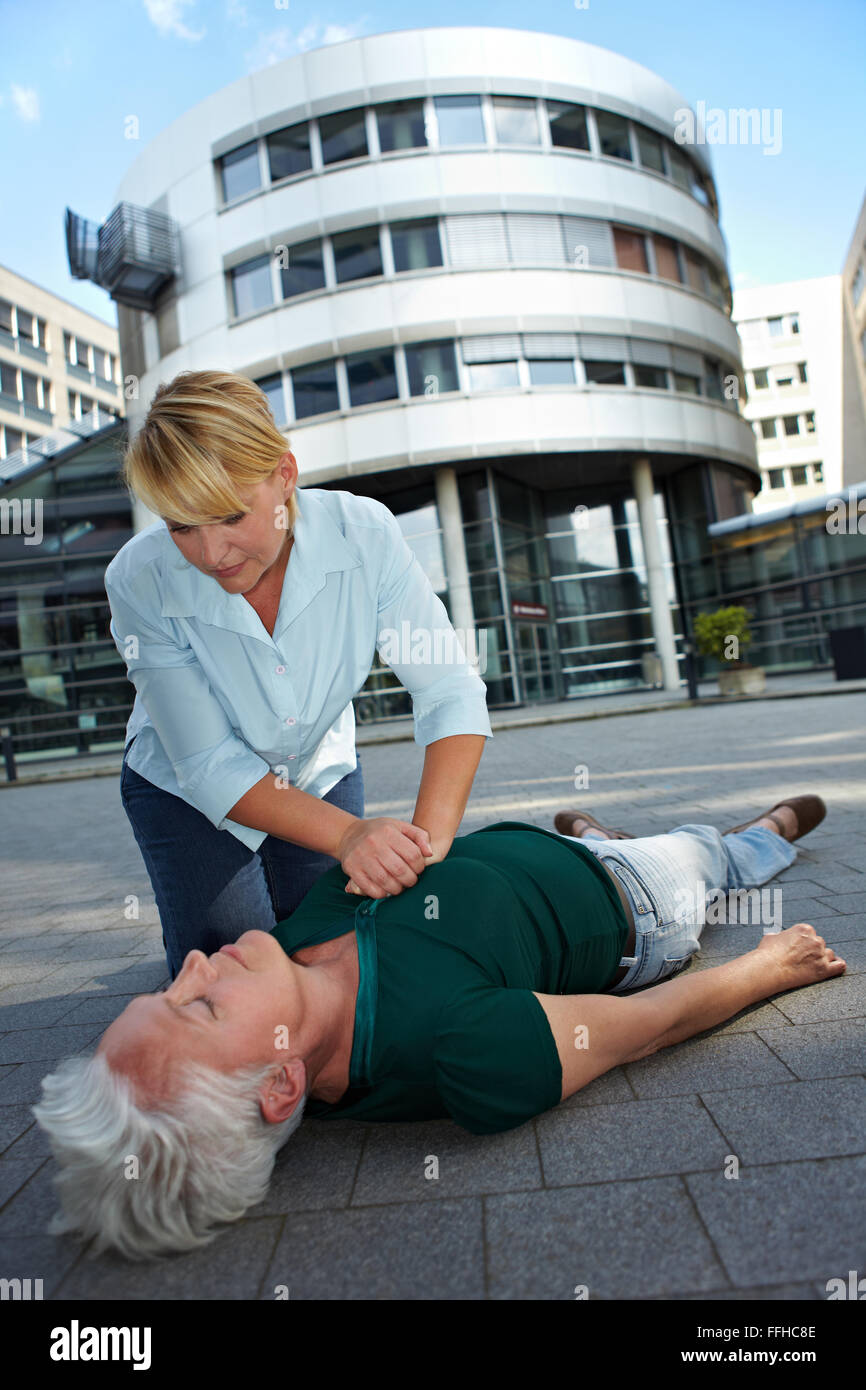 Passerby giving CPR to senior woman as First Aid Stock Photo