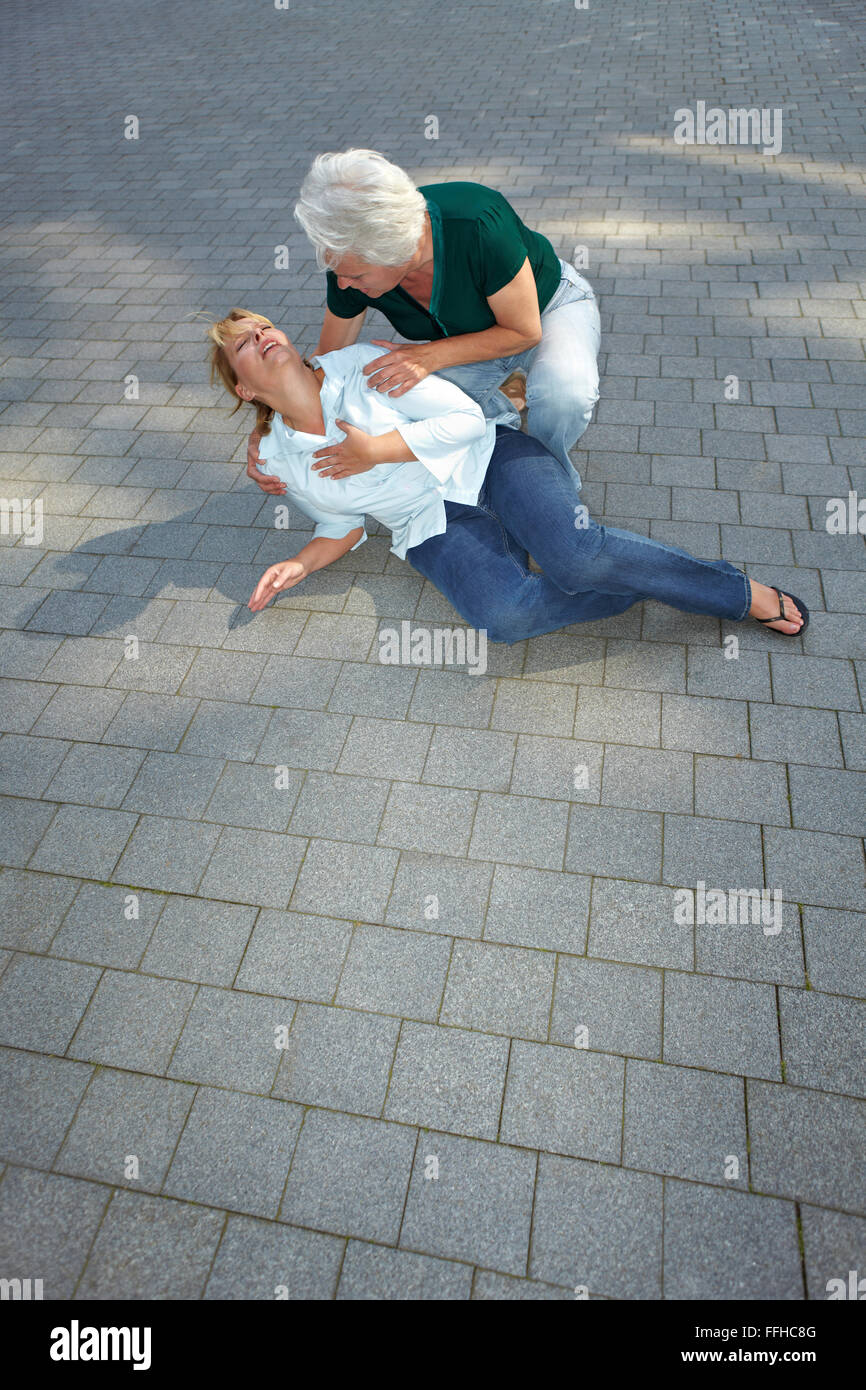 Senior woman helping passerby with heart attack in city Stock Photo