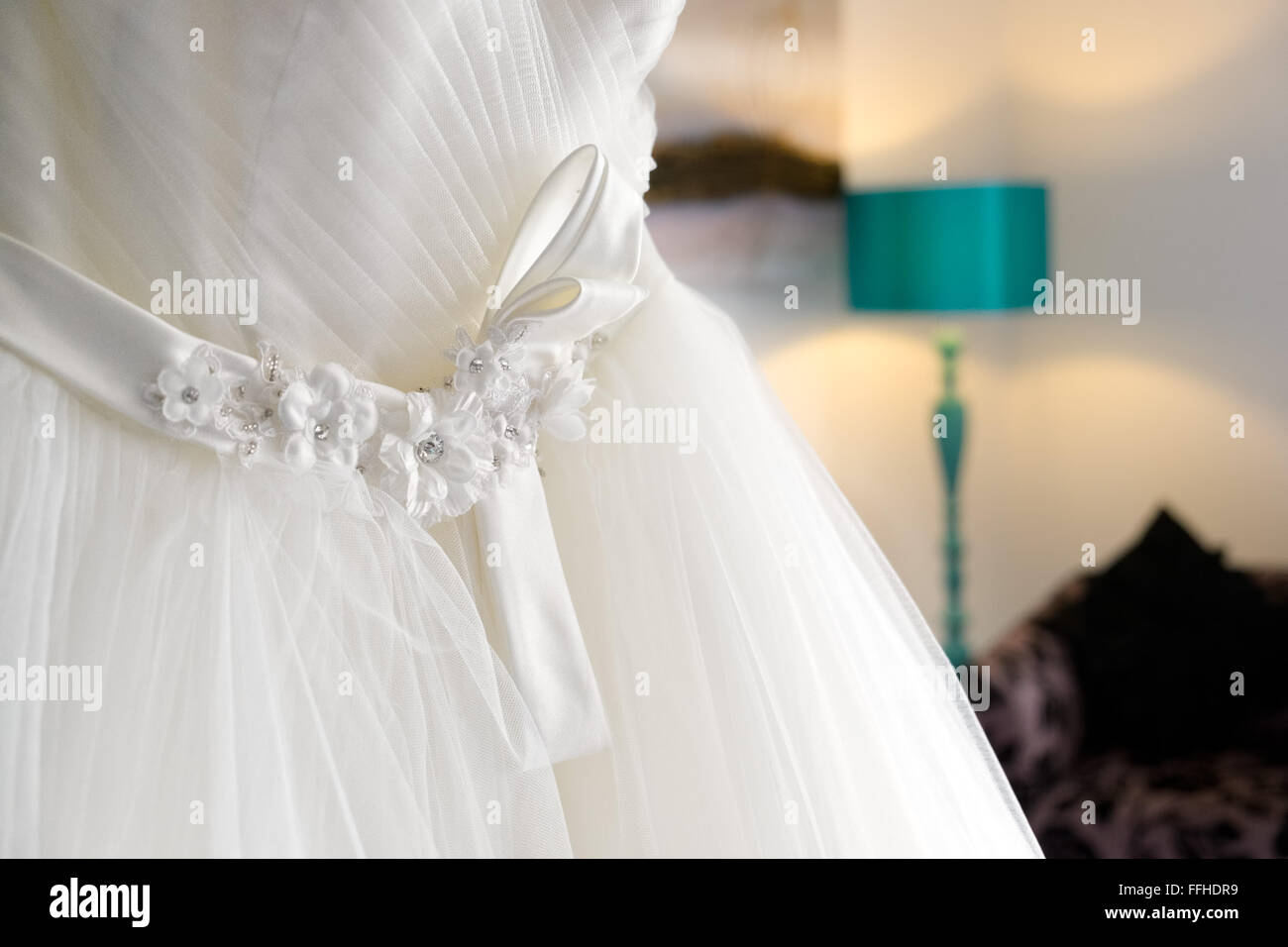 A traditional white wedding dress hanging in a bedroom waiting for a bride to put it on Stock Photo