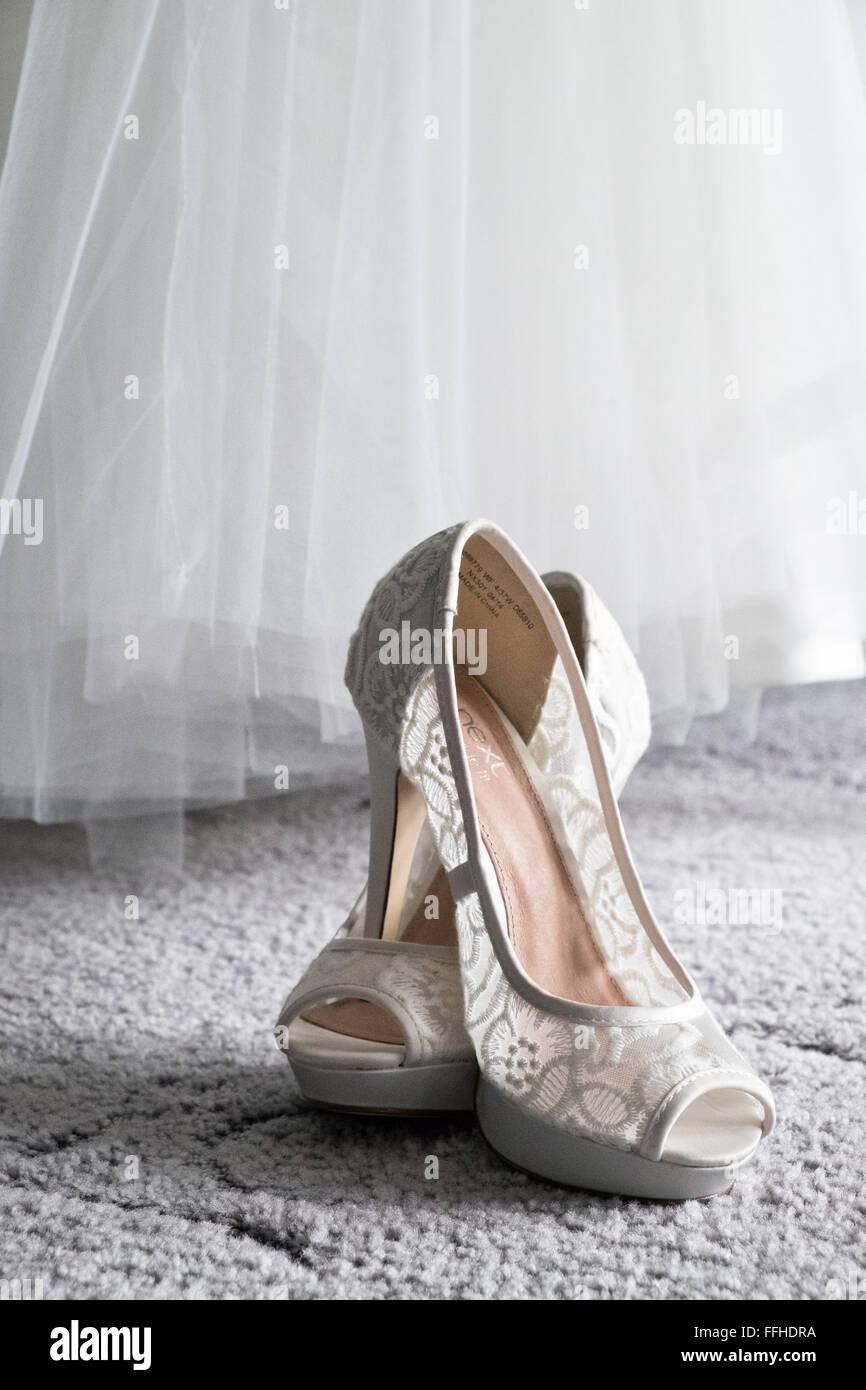 A brides shoes sit crossed, below her dress on carpet waiting to be worn during the wedding day Stock Photo