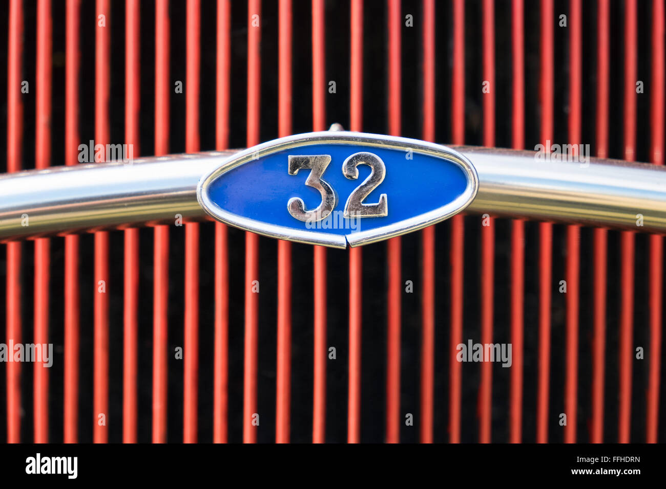 The number 32 within a blue plaque, part of a chrome bar in front of a bright red car grill Stock Photo