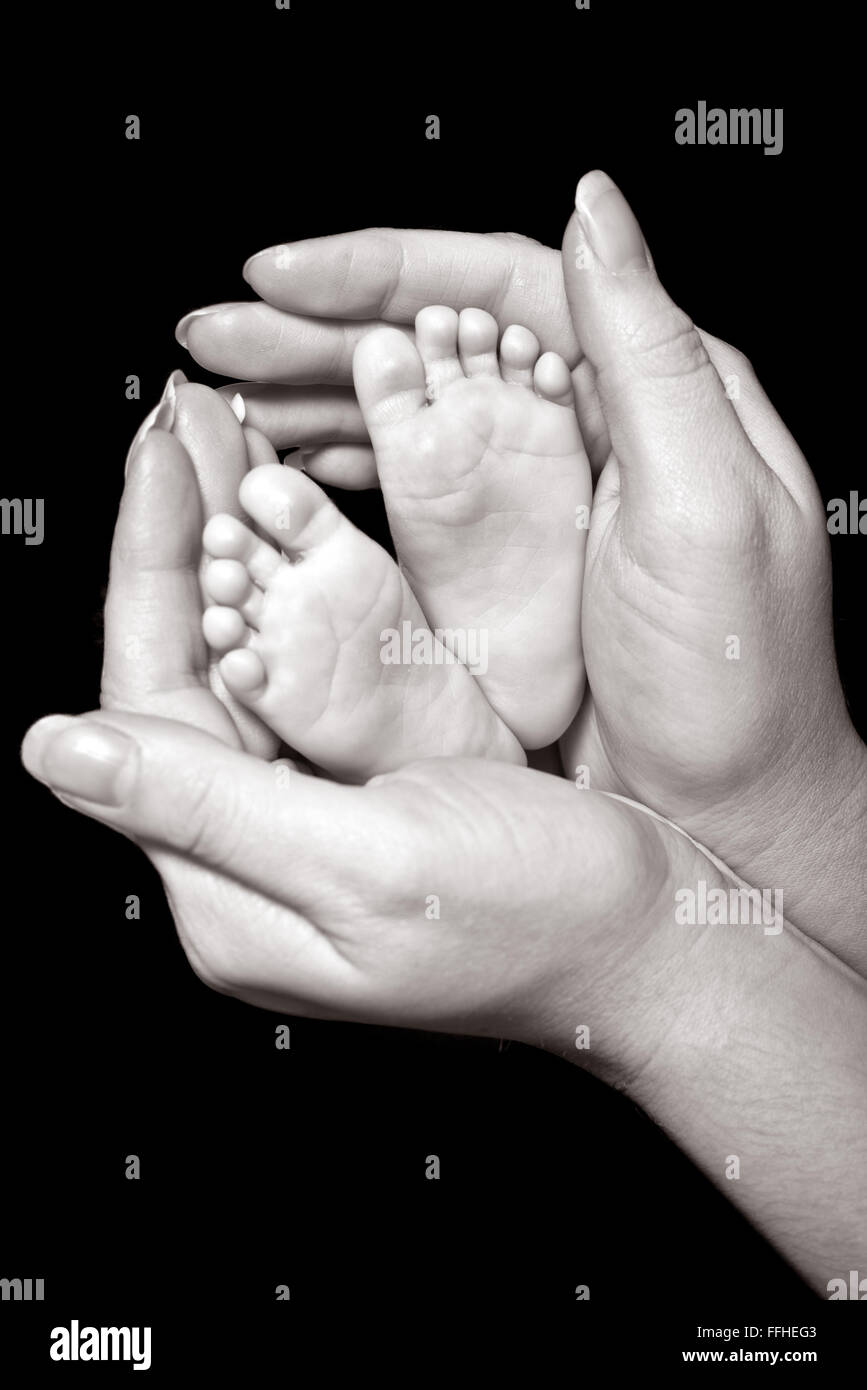 An image of the crossed feet of a newborn with wedding rings on its toes, cupped in its mothers hands Stock Photo