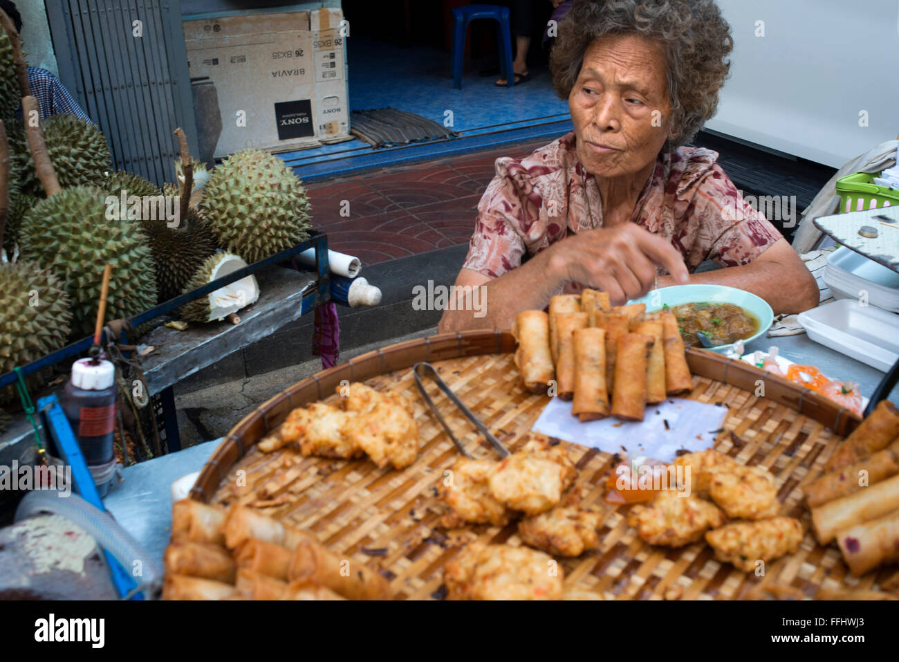 Woman selling pring rolls and durian fruits. Bangkok's Chinatown , Thailand. Market stall and street food being prepared in Chin Stock Photo