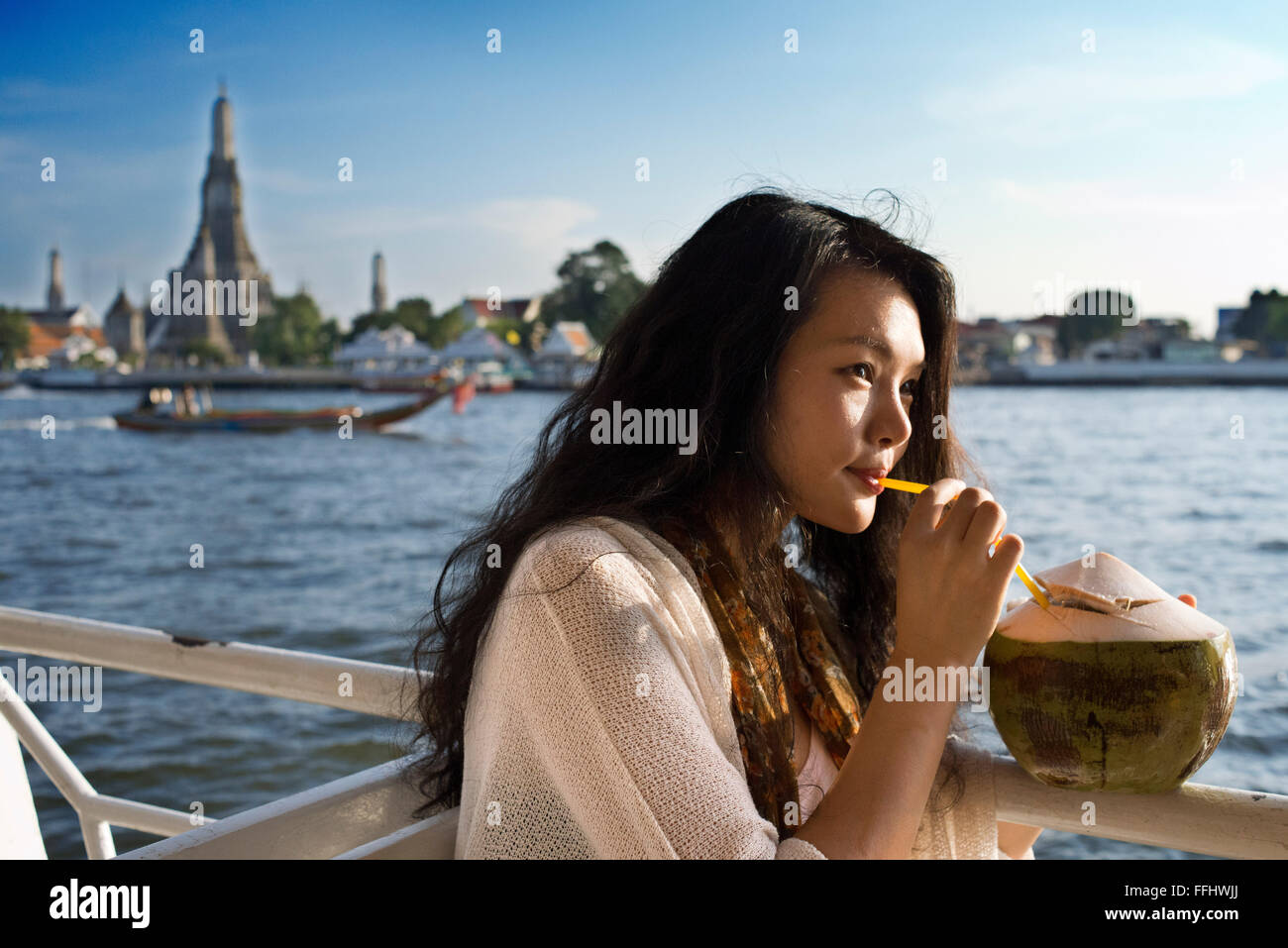 Romantic nice girl in a boat near Wat Arun Temple and Chao Praya River. Drinking a coconout. Chao Phraya Tourist Boat. The BTS S Stock Photo
