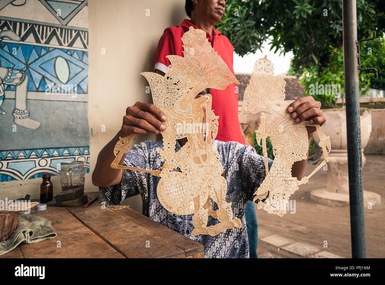 A craftsman at the Taman Sari Palace in Yogyakarta, Indonesia displaying two unfinished Wayang puppets sculpted in buffalo skin. Stock Photo