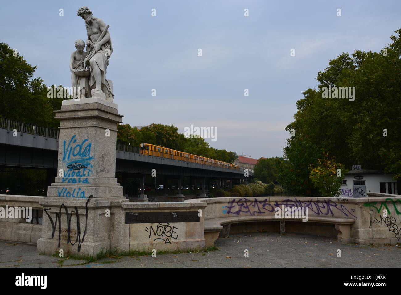 Graffiti covers a railing, bench, and statue base next to a train stop in Berlin, Germany. Stock Photo