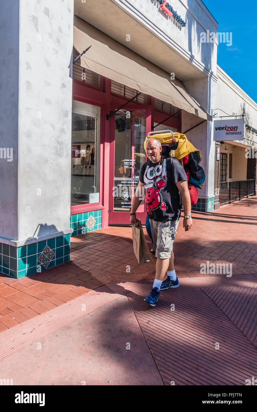 An older transient male backpacker carries his world possessions on his back as he walks up State Street in Santa Barbara, CA. Stock Photo