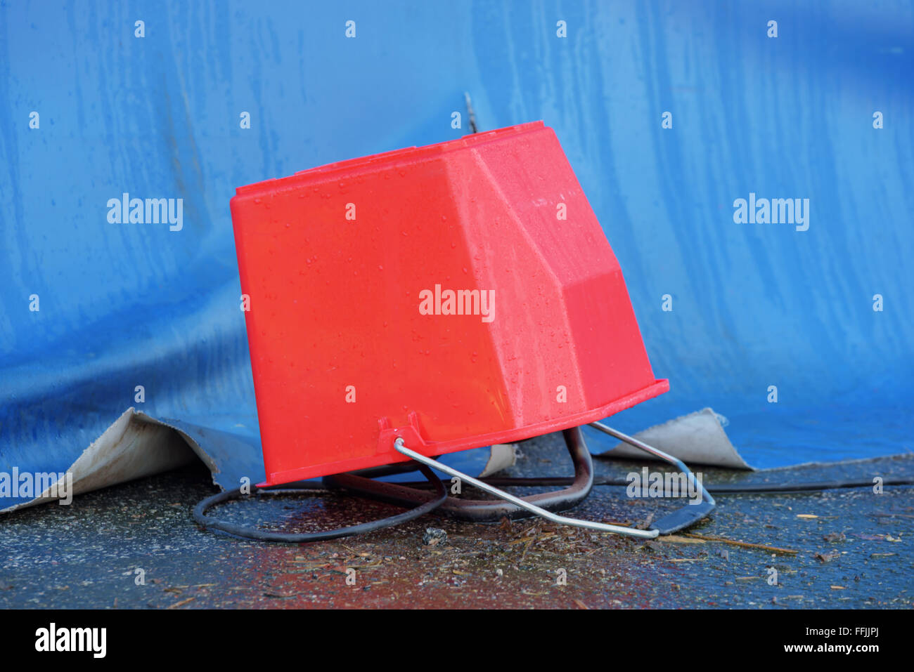 A makeshift weather shelter made of a red plastic bucket. An electric outlet is under the bucket and a cable is going from the i Stock Photo