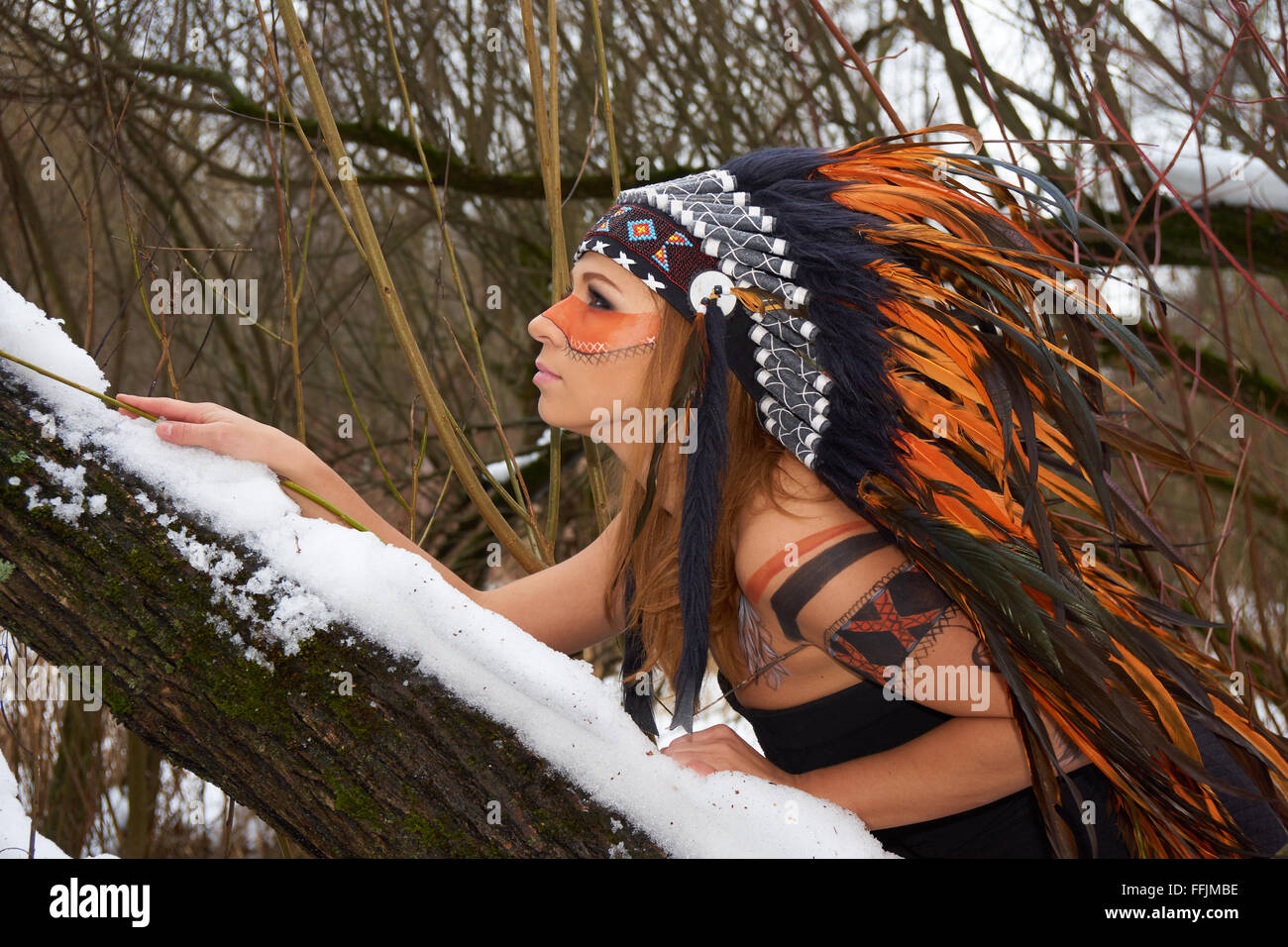 Girl in native american headdress climbs tree Stock Photo