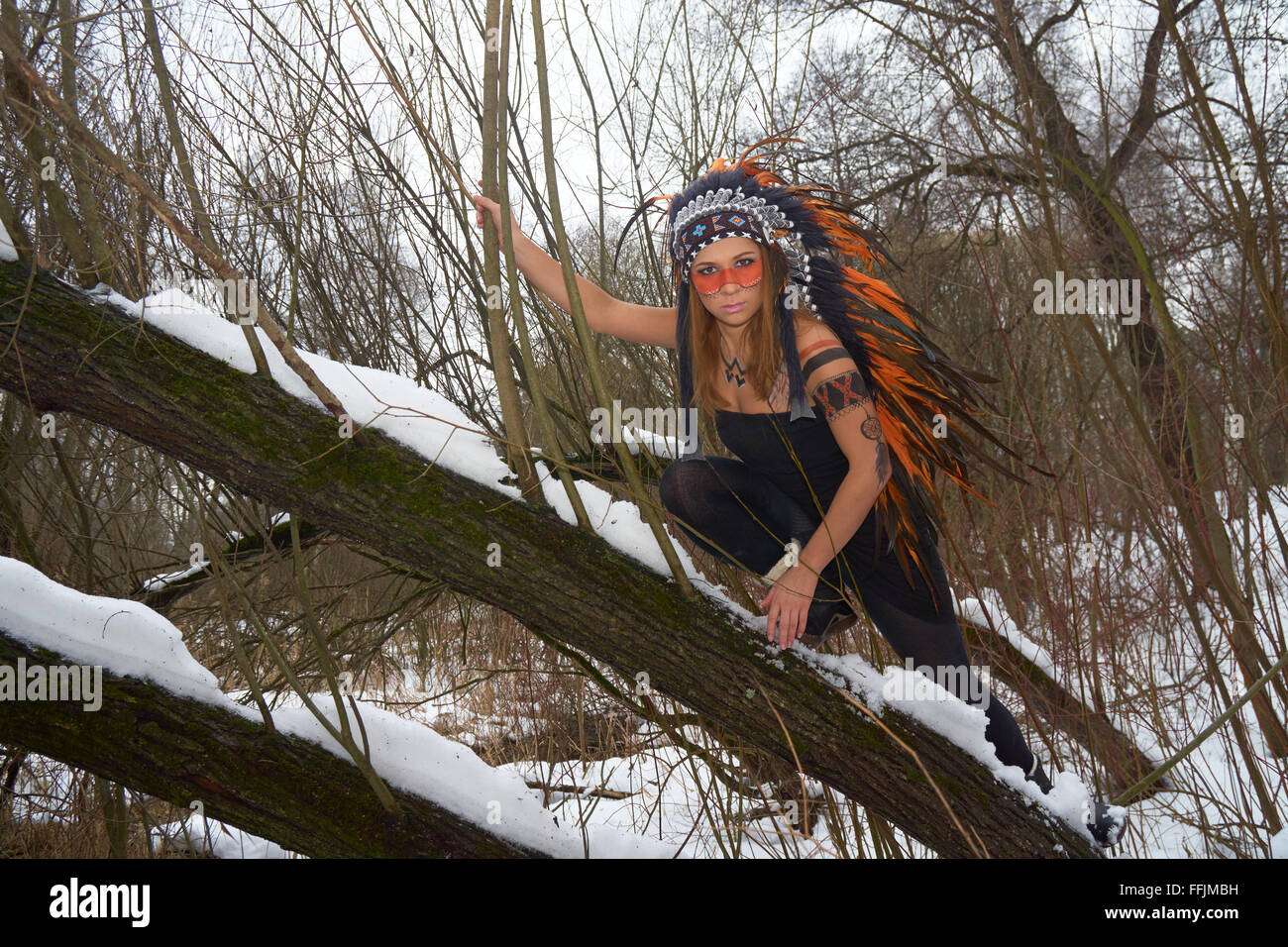 Girl in native american headdress climbs tree Stock Photo