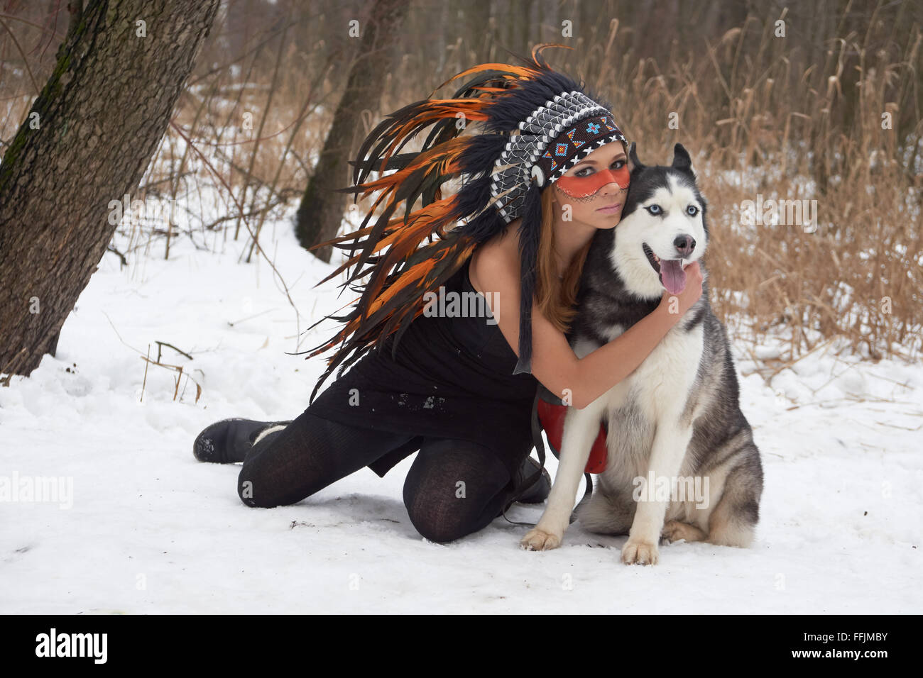 Girl in native american headdress embraces her Siberian Husky Stock Photo