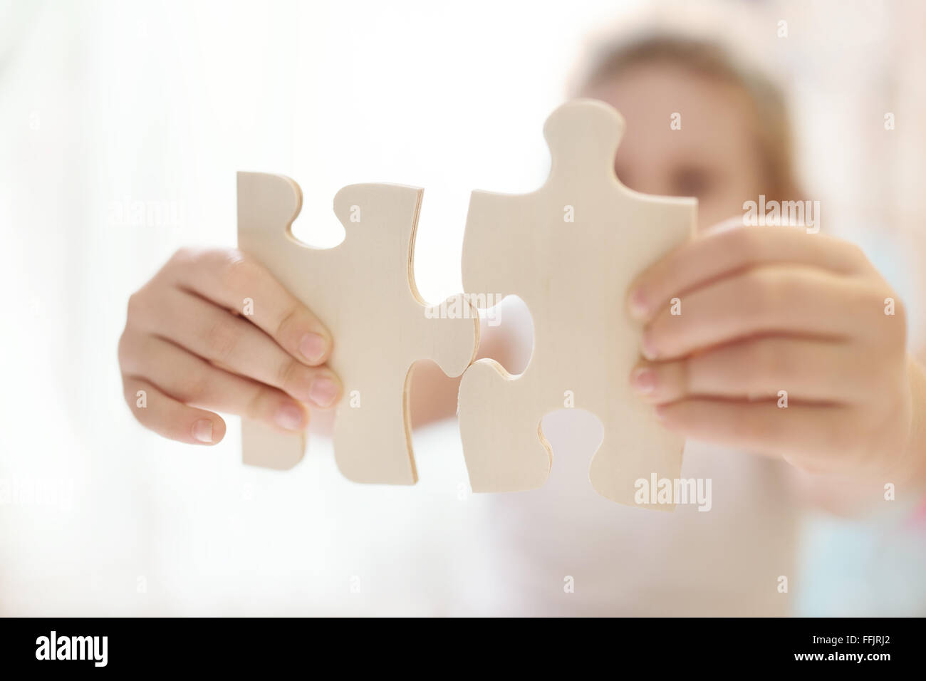 Child girl holding  two big wooden puzzle pieces. Hands connecting jigsaw puzzle. Close up photo with small dof. Education and learning concept. Stock Photo