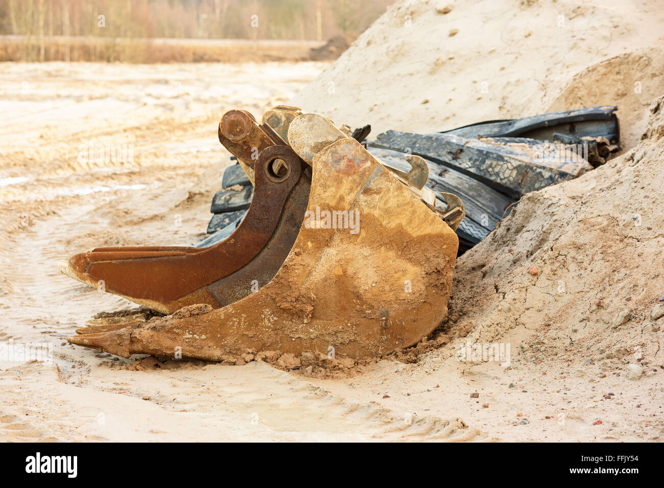 Two excavator scoops, one inside the other, at a sandy and muddy construction site. Stock Photo