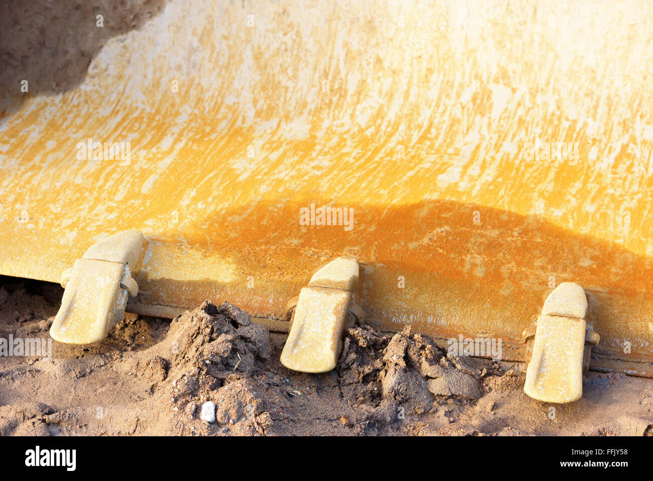Close up detail of a front loader bucket or scoop. Ground is wet and muddy. Scoop is rusty and well used. Stock Photo