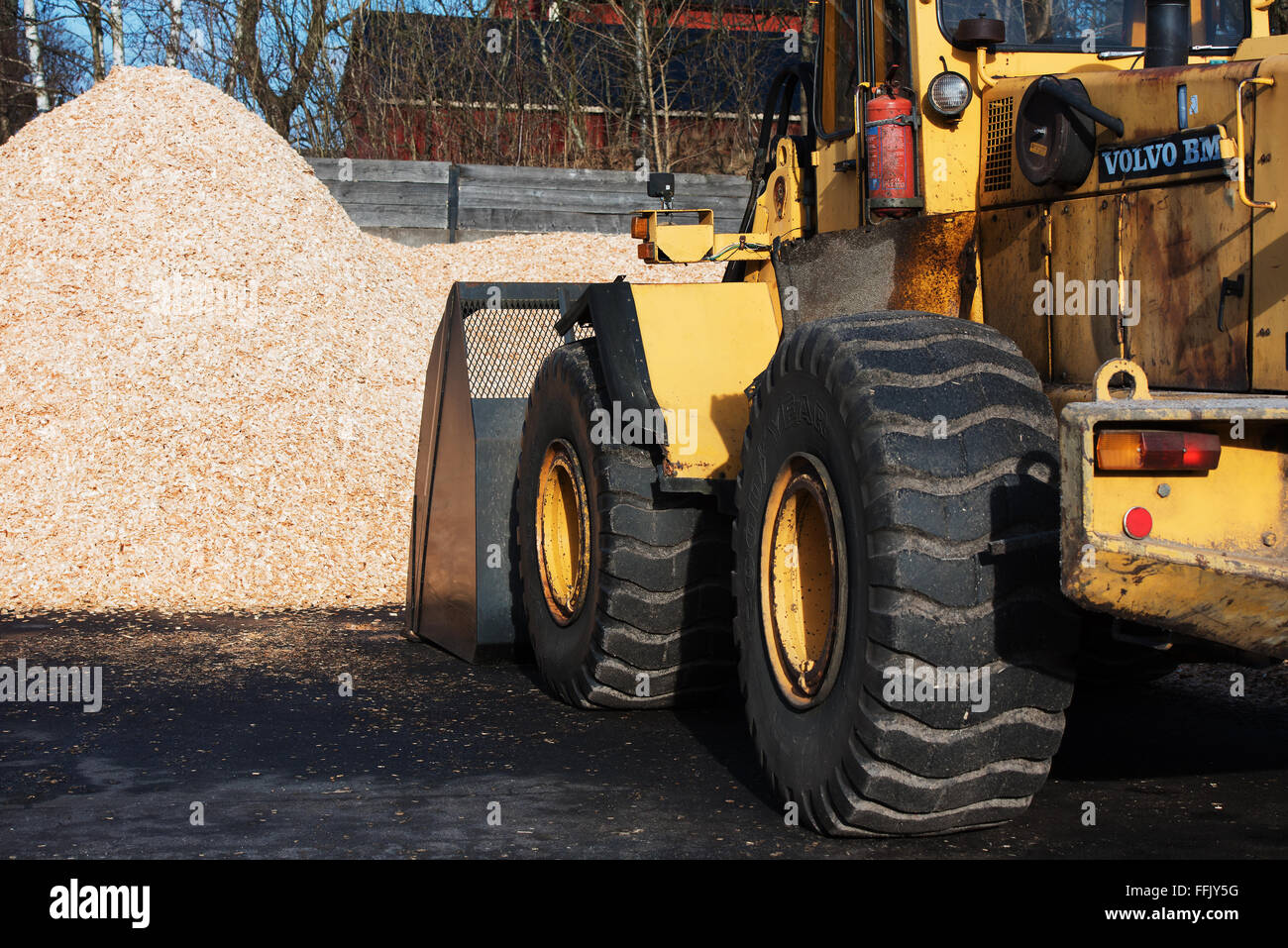 Brakne-Hoby, Sweden - February 07, 2016: A yellow Volvo BM front loader with scoop down loading biofuel from a pile of woodchips Stock Photo