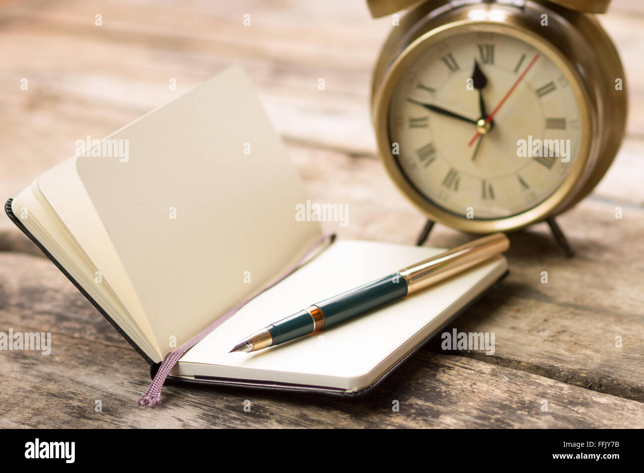 Open Notebook With Fountain Pen And Alarm Clock On Wooden Desk