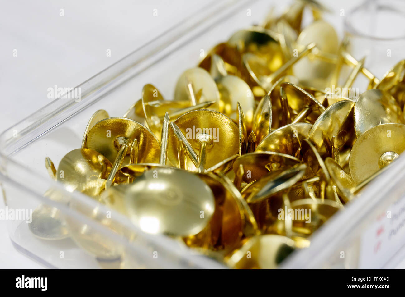 close up plastic box filled with brass drawing pins/thumb tacks England Stock Photo