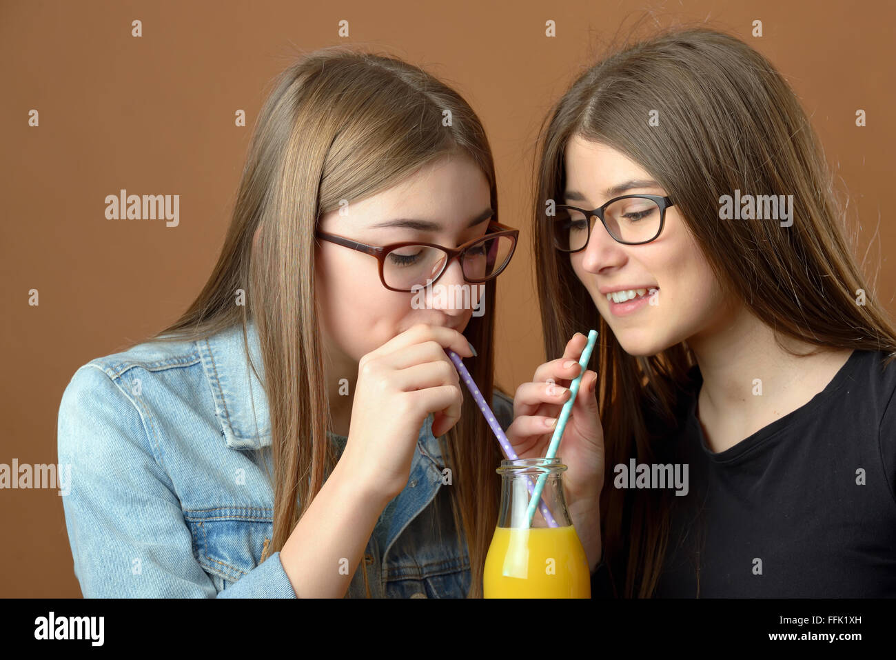 Girls sharing an orange juice drink Stock Photo