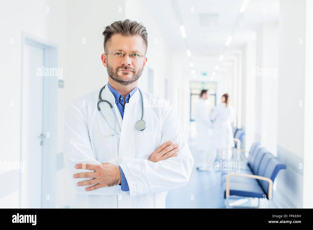 Portrait of doctor with arms crossed in hospital corridor Stock Photo