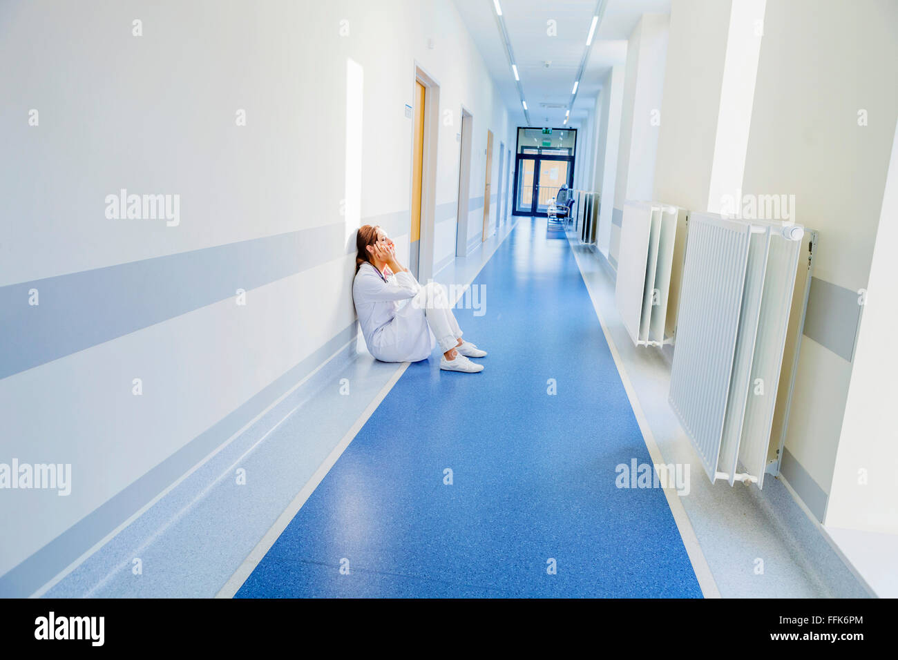 Overworked healthcare worker sitting on floor in hospital corridor Stock Photo