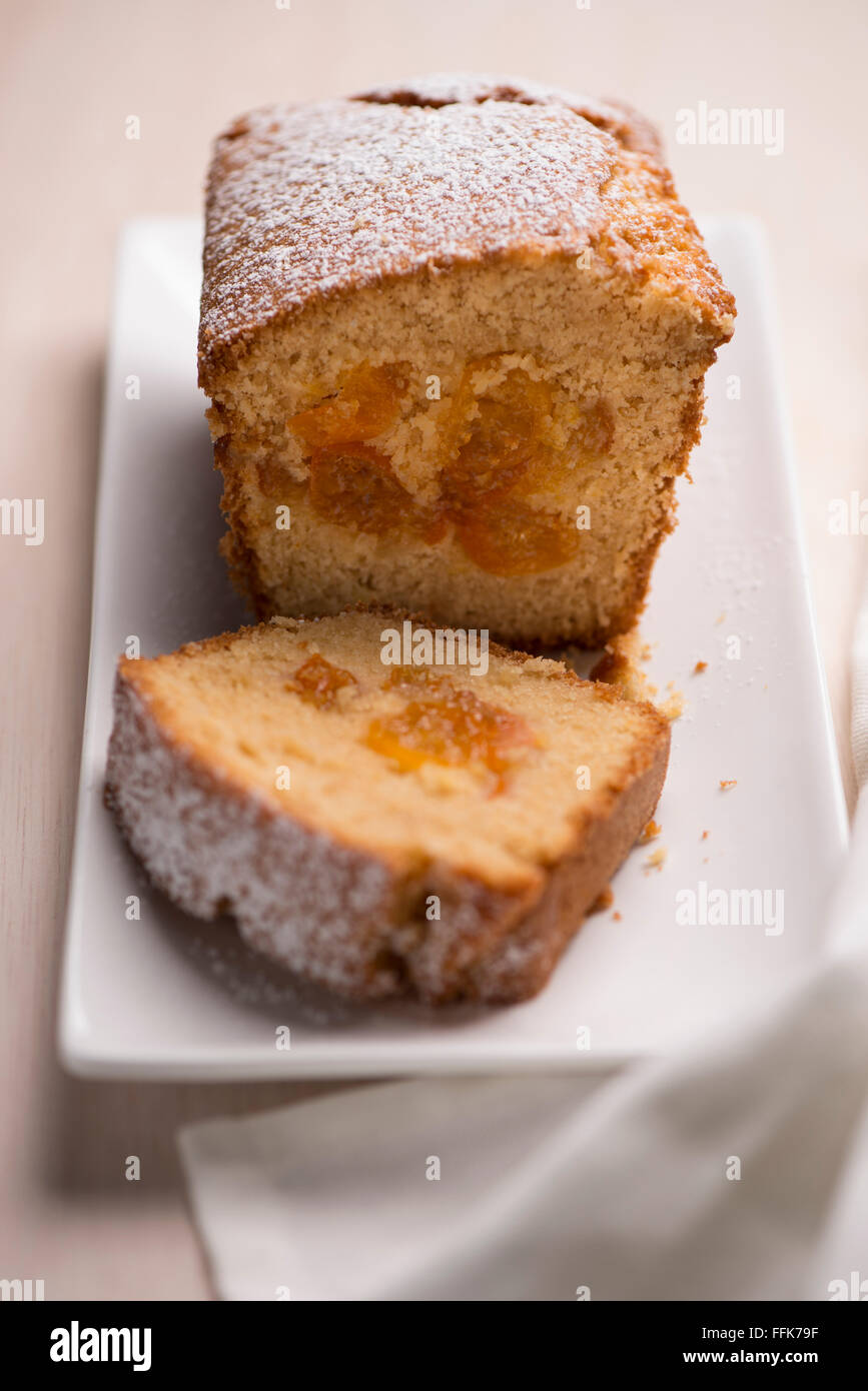 One kumquat cake loaf topped with icing sugar, one slice out, on a white plate Stock Photo