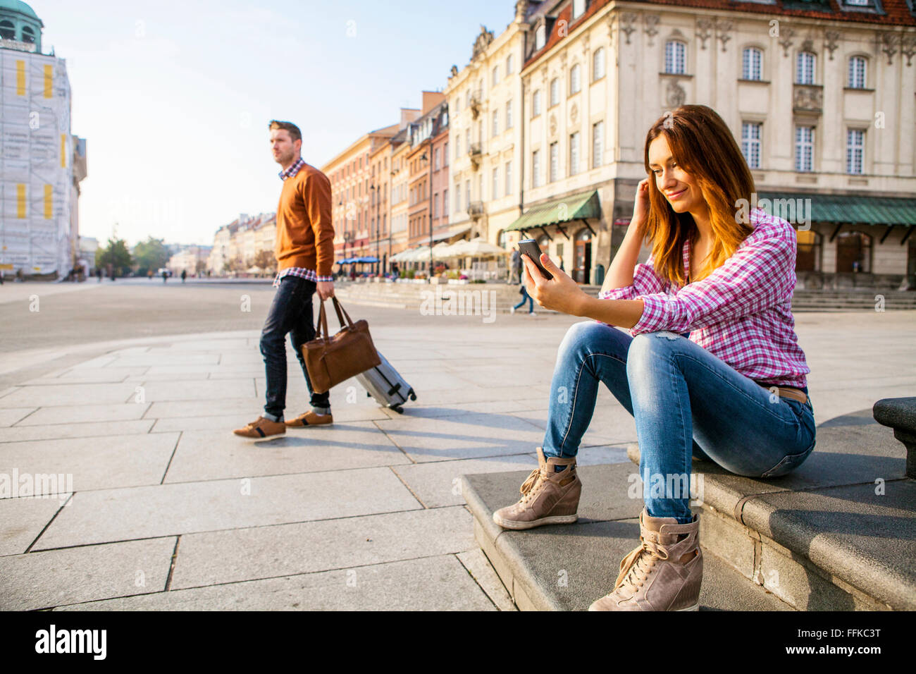 Mid adult woman using smart phone with man in background Stock Photo