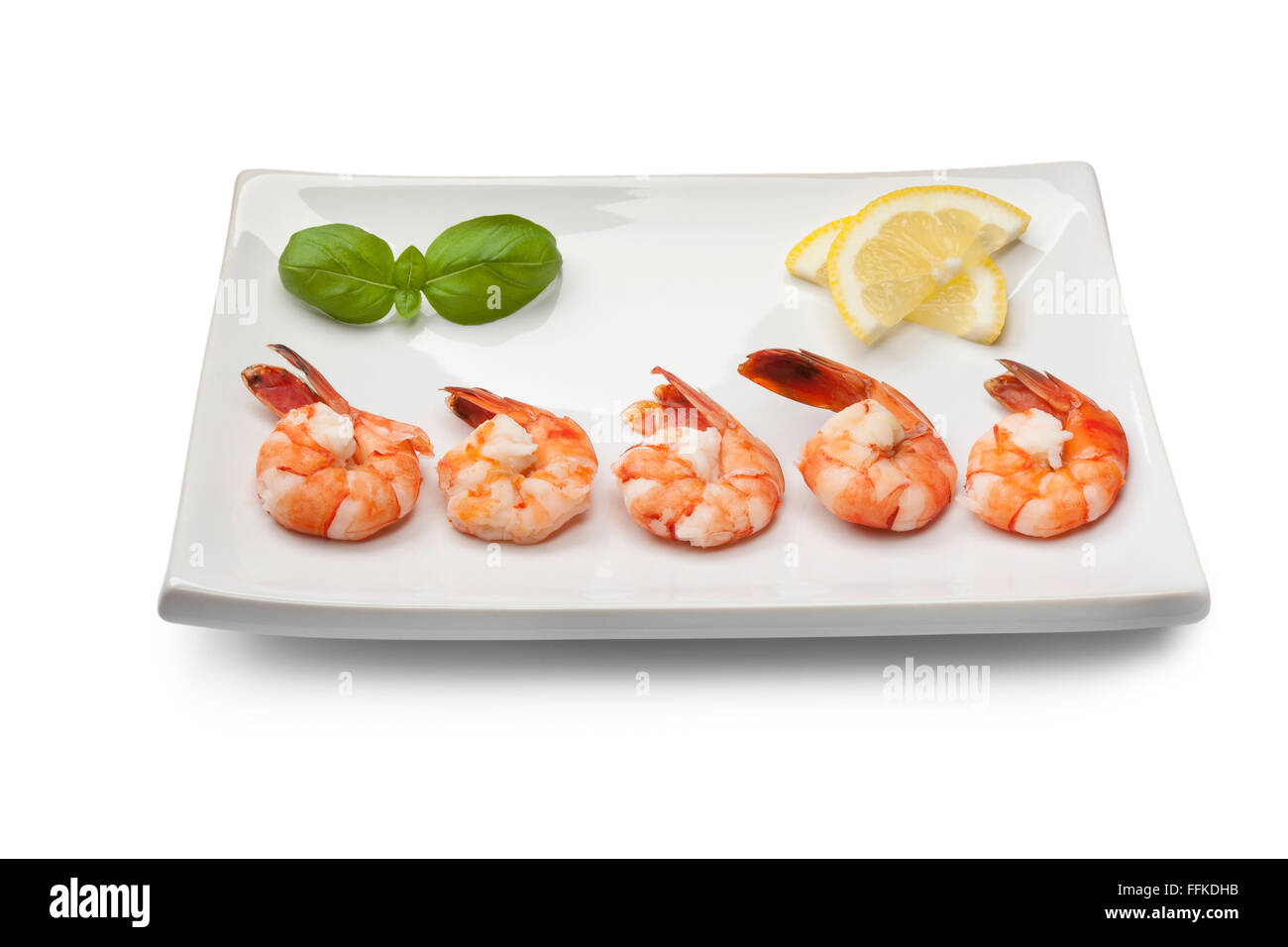 Cooked shrimps with lemon and basil leaves on a dish on white background Stock Photo