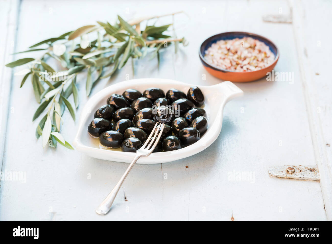 Black olives in white ceramic plate, branches and spices over light