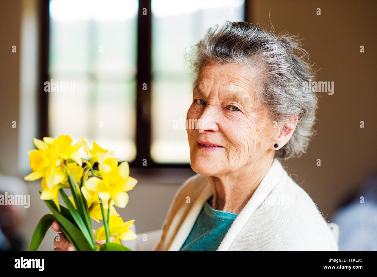 Senior woman by the window holding bouquet of daffodils Stock Photo