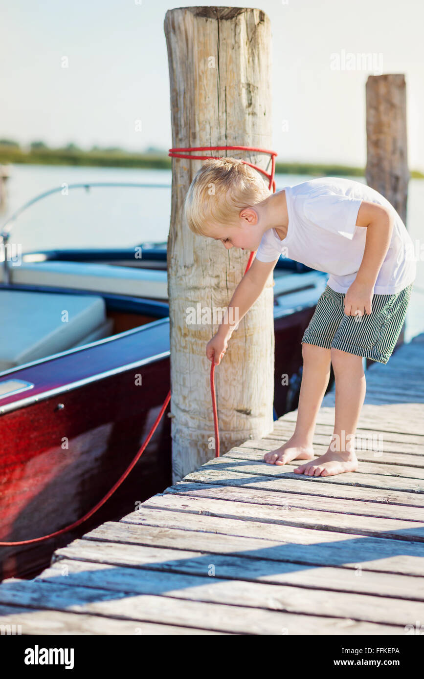 Boy on the pier with motorboat, sunny summer Stock Photo