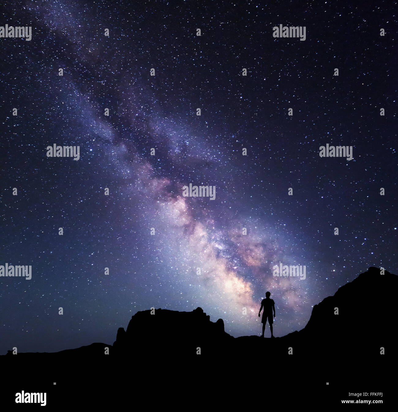 Landscape with Milky Way. Night sky with stars and silhouette of a standing happy man on the mountain. Stock Photo