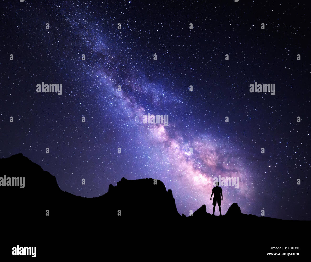 Landscape with Milky Way. Night sky with stars and silhouette of a standing happy man on the mountain. Stock Photo