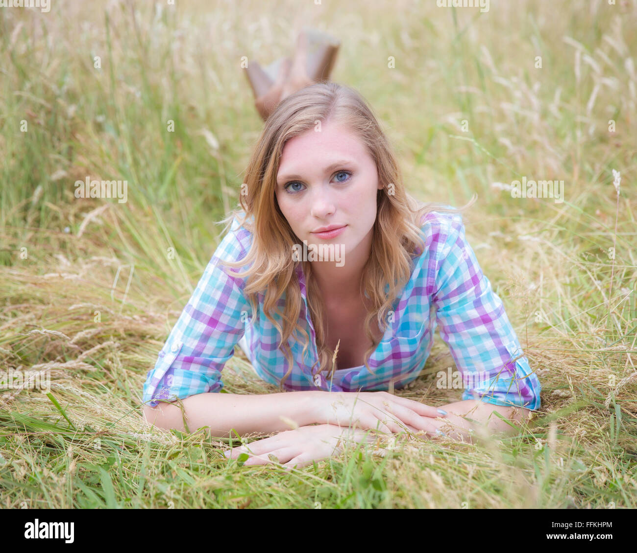 Beautiful blond woman in a tall grass laying on her stomach Stock Photo