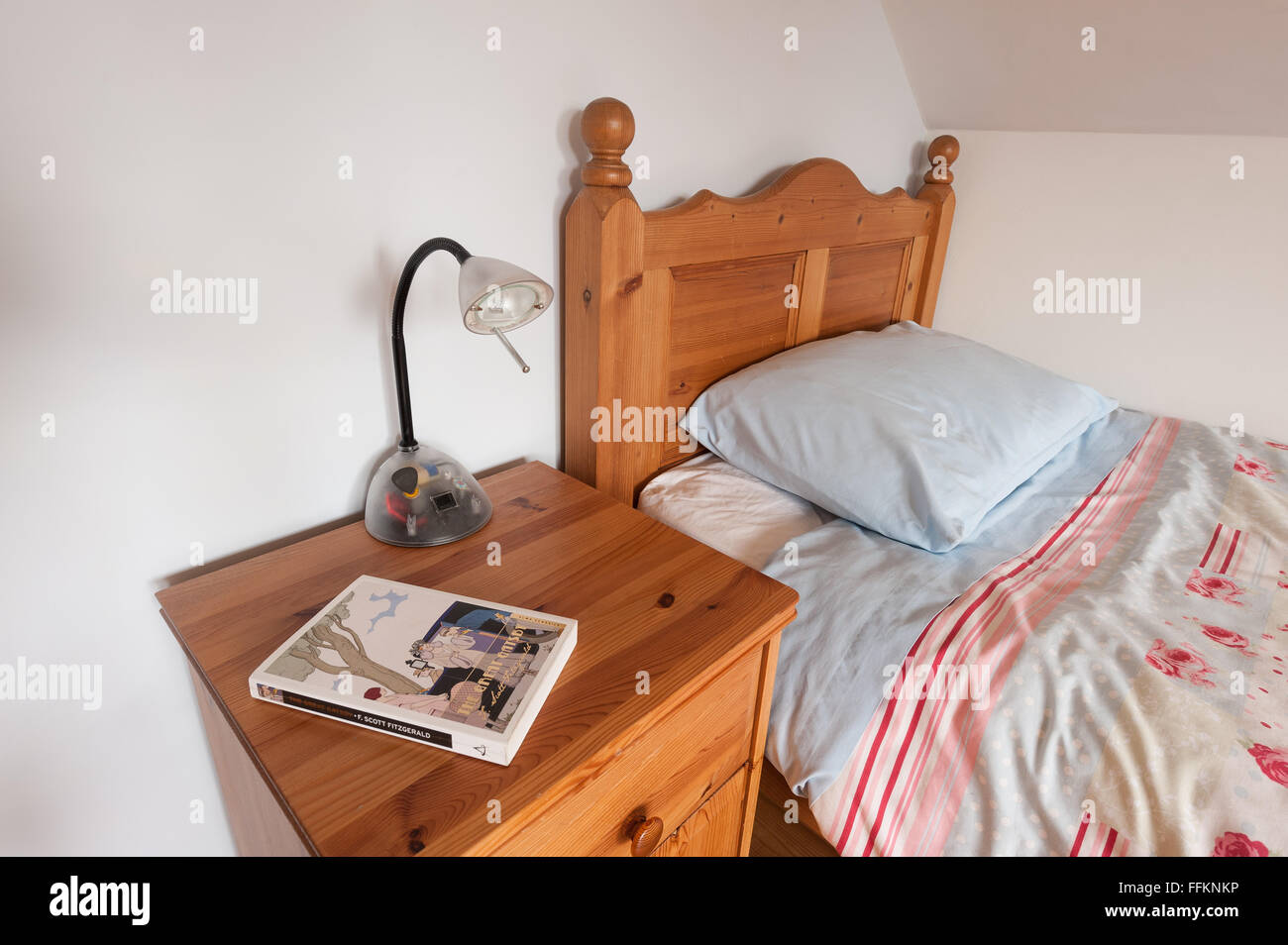 neat wooden pine bed and duvet with cabinet and lamp ready for a good bedside read of a novel Stock Photo