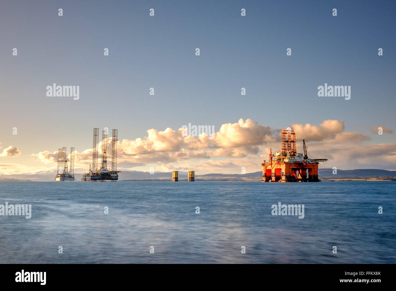 Three oil rigs float in the Cromarty Firth in northern Scotland as a seagull flies just above the horizon. Stock Photo