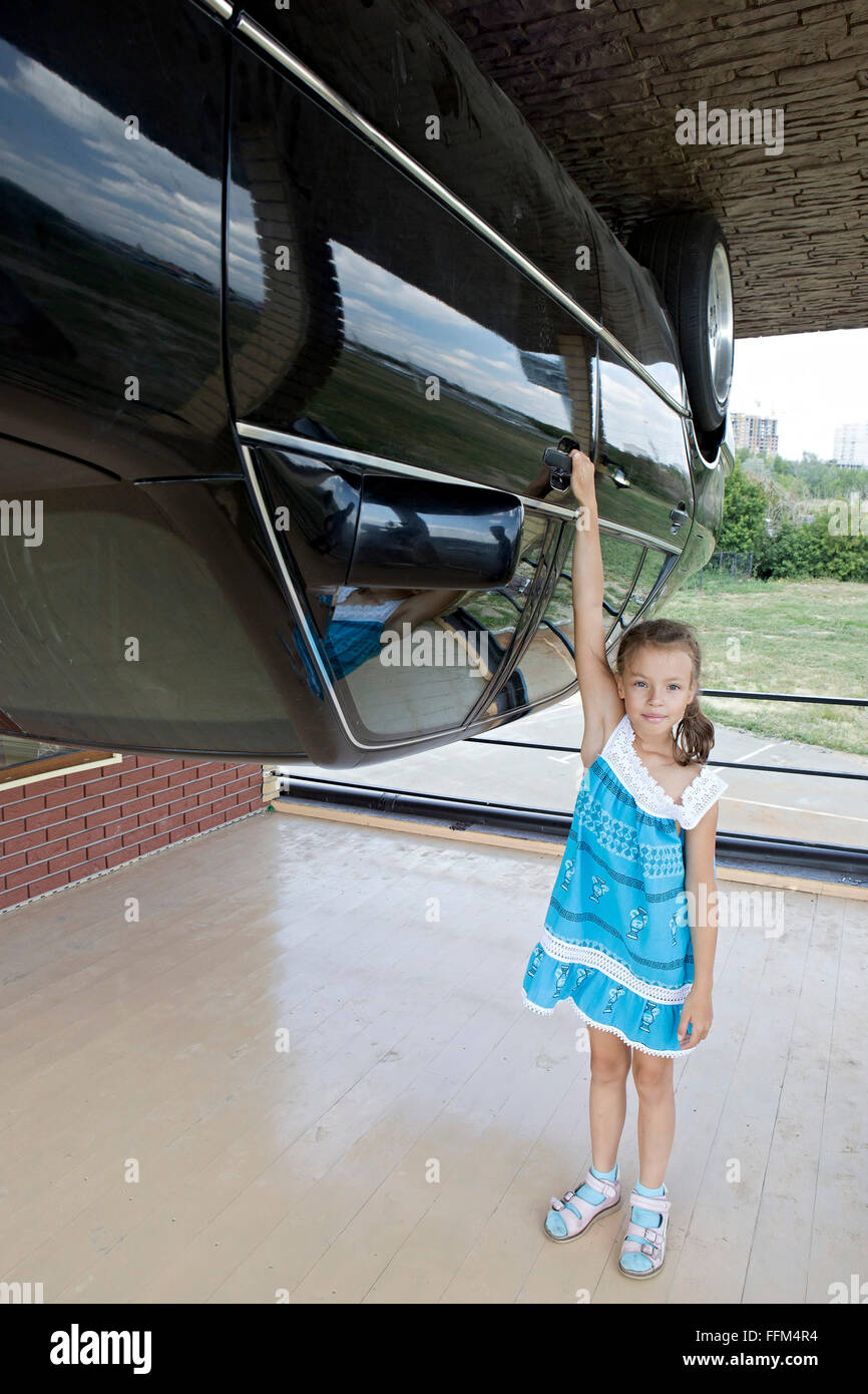 Little girl with the car in attraction Inverted house. Stock Photo