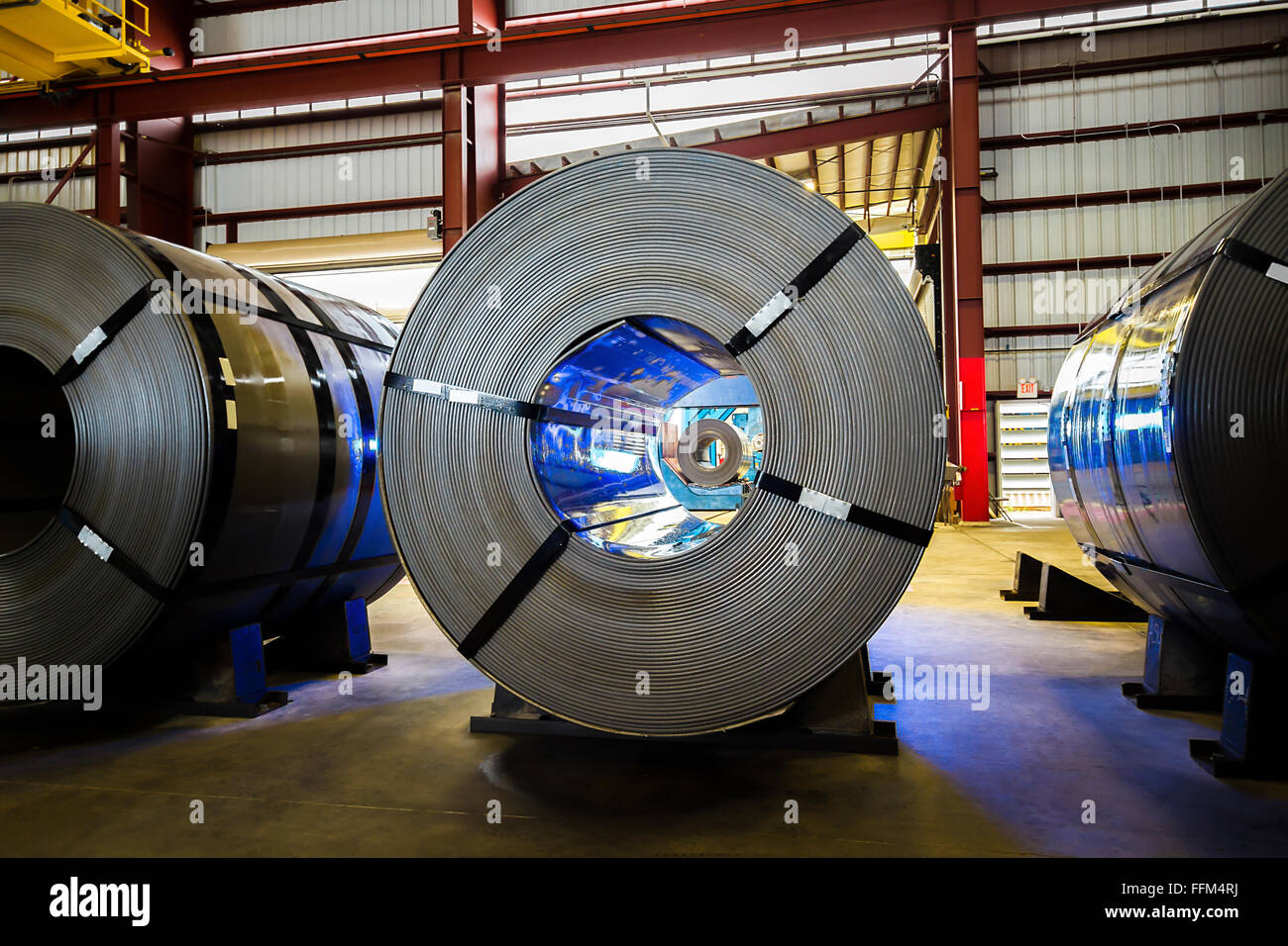 3 master coils on steel chocks in warehouse with coil seen inside eye of coil and blue reflected light showing crane rails and e Stock Photo