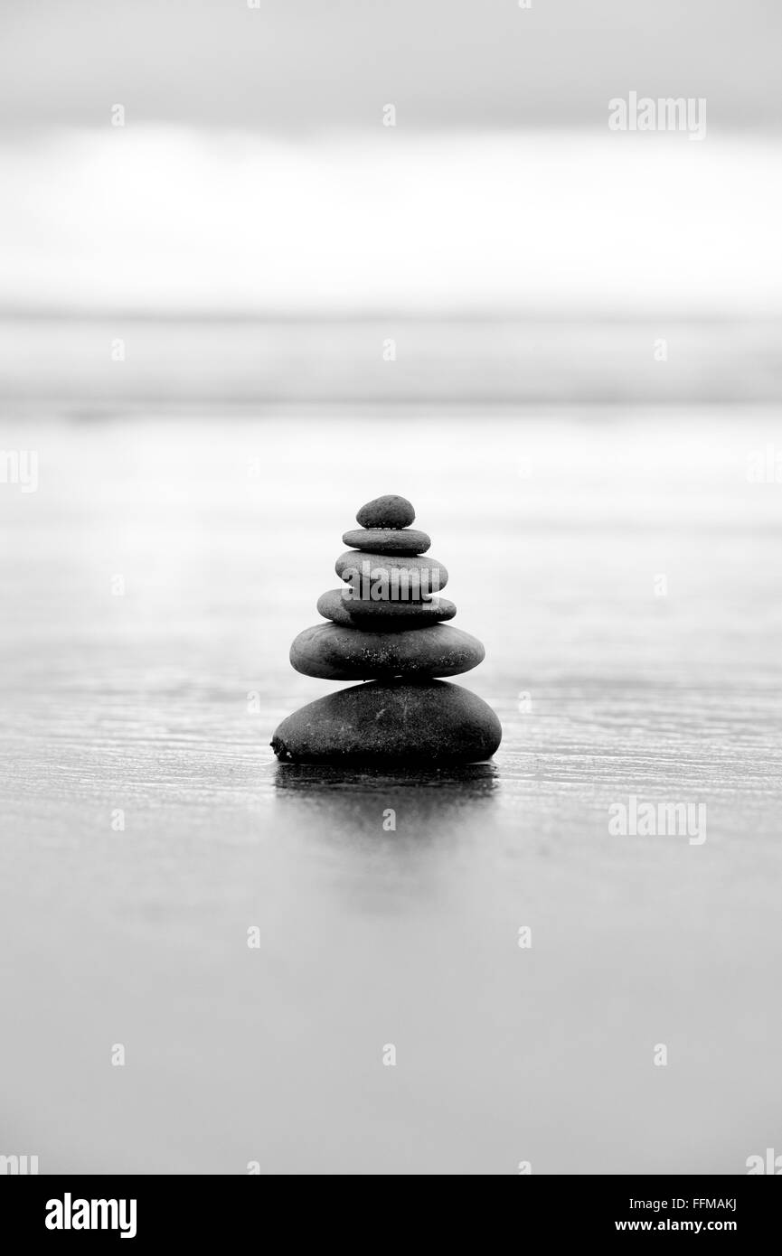 Pebbles balancing on a stormy beach in the early morning light. Black and White.  Selective focus Stock Photo
