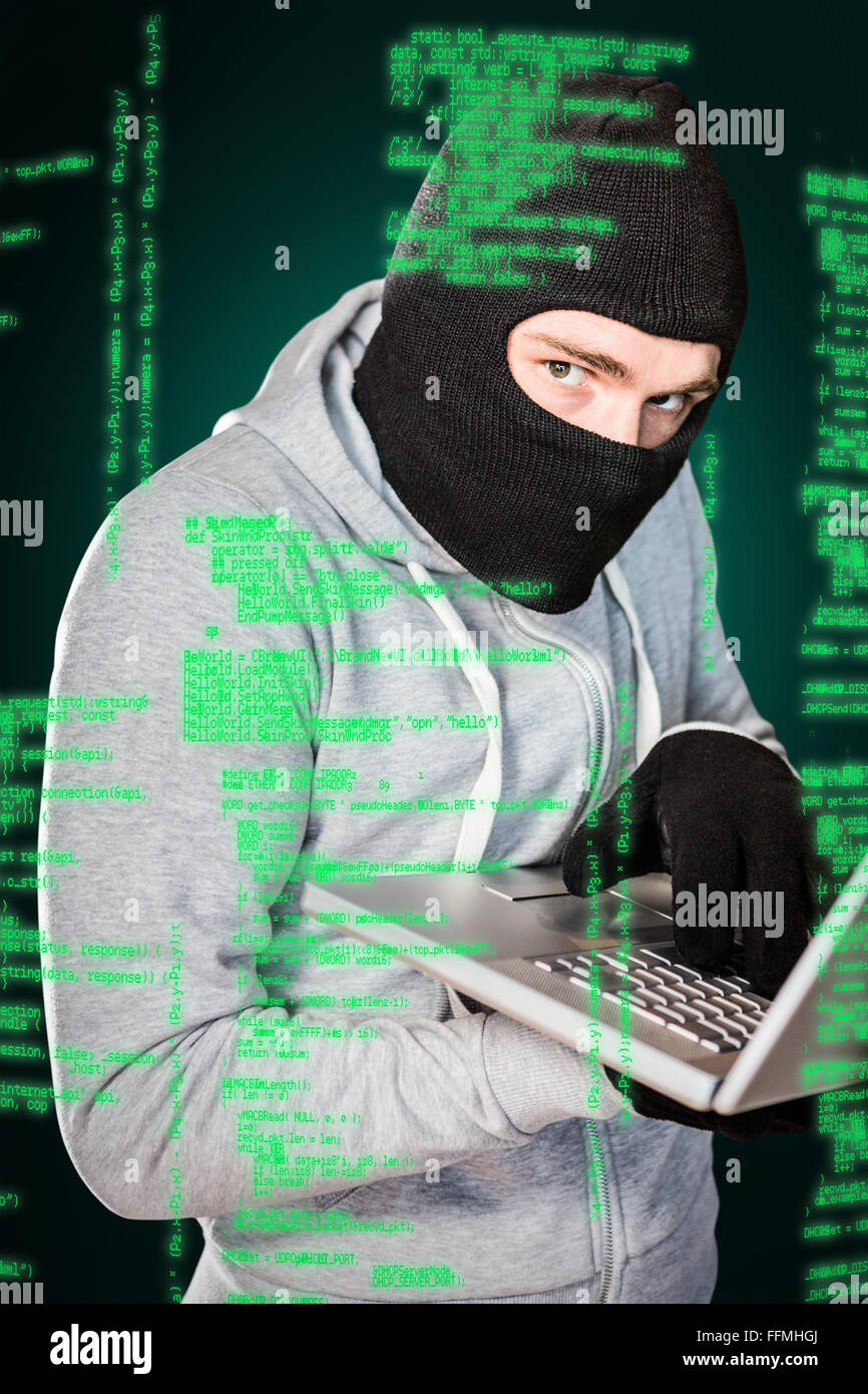 Composite image of focused thief with hood typing on laptop Stock Photo