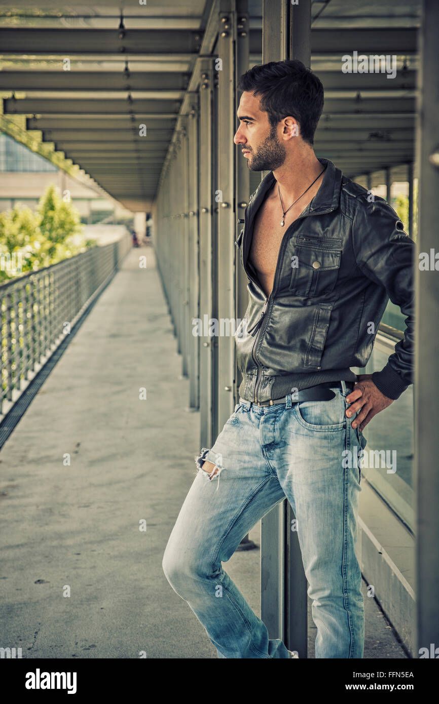 Side view of young bearded man standing on balcony and looking down sadly Stock Photo