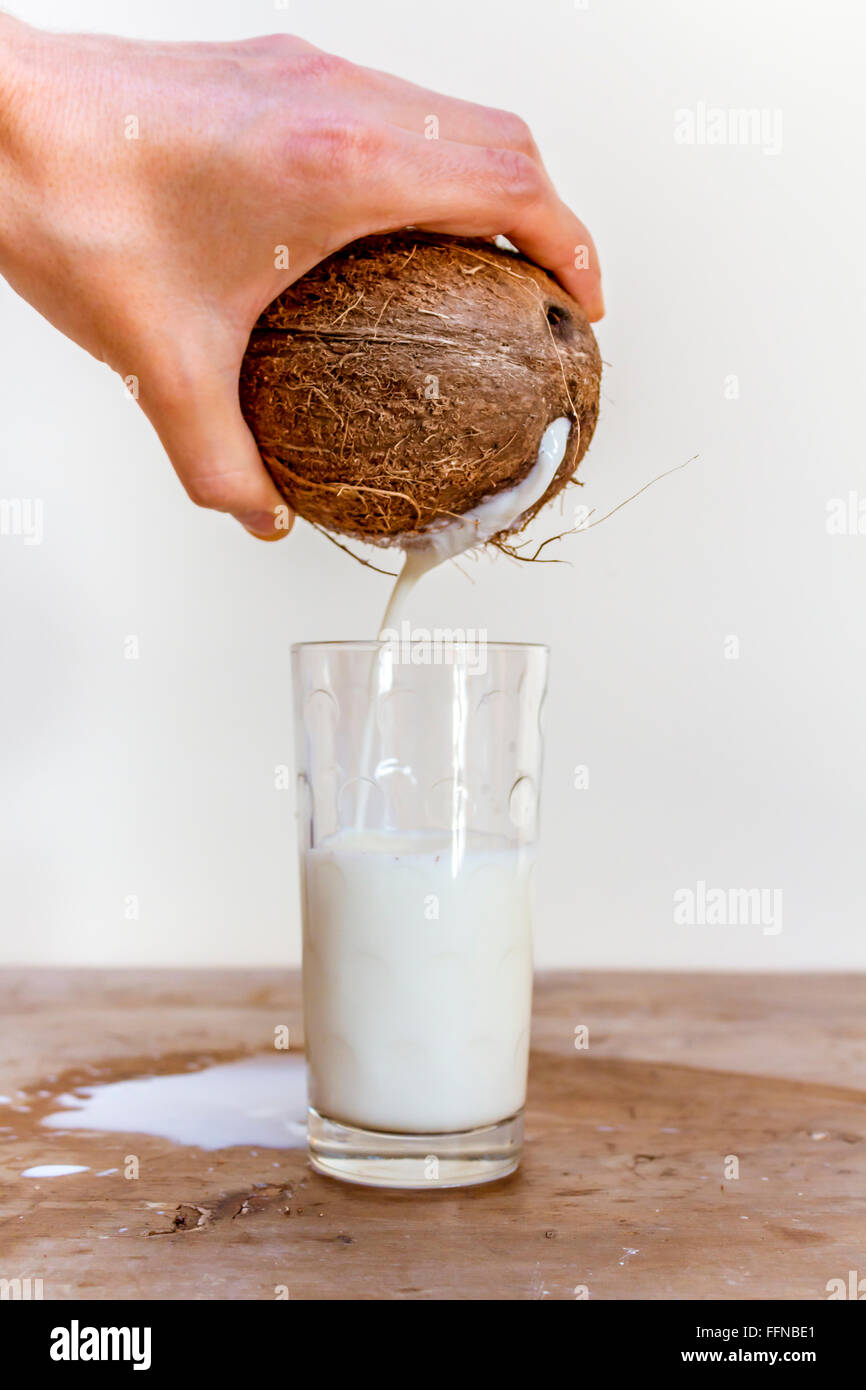 Pouring milk from a coconut into a glass on a wooden table Stock Photo