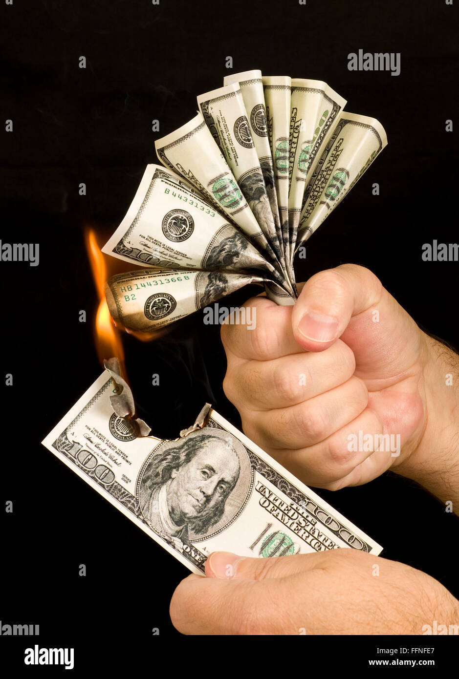 Money to Burn.  A man uses a one hundred dollar bill to set fire to the hand full of one hundred dollar bills in his other hand. Stock Photo