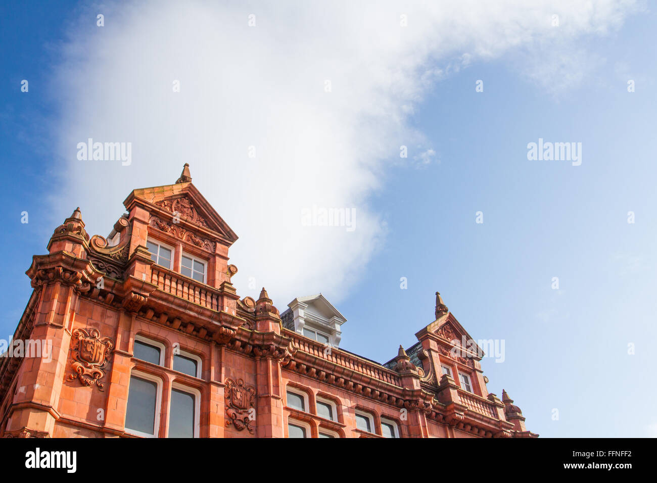 The front of an old building with red brick and ornate masonry. The facade of a period building and roof with blue sky for copy Stock Photo