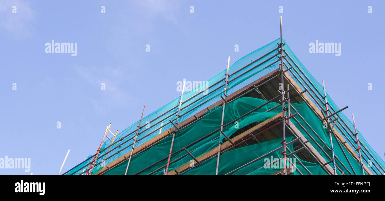 A tall building surrounded by scaffolding during construction work and under a blue sky. Stock Photo